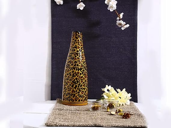A brown ceramic handmade vase with a leopard print design, placed on a beige textured surface, with a white and gold floral arrangement in front of it against a dark background.