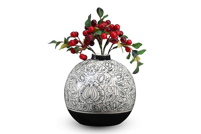 A handmade black ceramic vase with a floral design, containing real red berries.