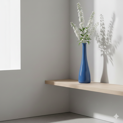 Blue vase with white flowers on a wooden shelf against a gray wall.