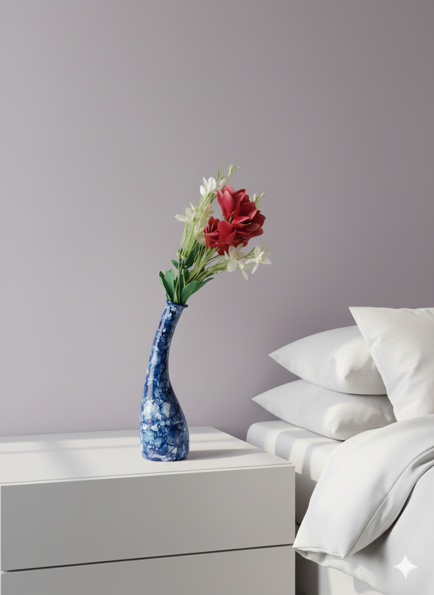 Blue vase with flowers on a nightstand next to a bed with white pillows and bedding.