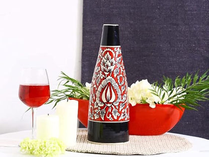 A handmade black and red ceramic Mughal vase with floral patterns, displayed on a table with a red bowl of popcorn, greenery, and a glass of red wine in the background.