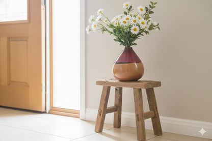 Vase with flowers on a wooden stool in a room with a door and wall.