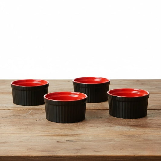 Four black ramekins with red interiors on a wooden surface