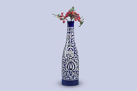 A handmade blue ceramic vase with floral patterns and a glossy finish, containing a bunch of red berries.