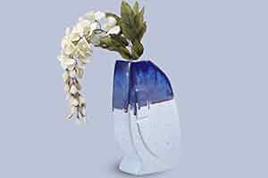 A handmade ceramic vase with blue and white matte finish, featuring a woven branch of flowers on top.