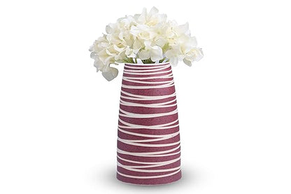 A handmade pink ceramic vase with strip patterns, featuring a glossy finish and containing white flowers.