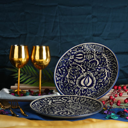 A set of two blue ceramic handmade stoneware plates with a Mughal quarter plate design, displayed on a table with golden wine glasses and decorative elements.